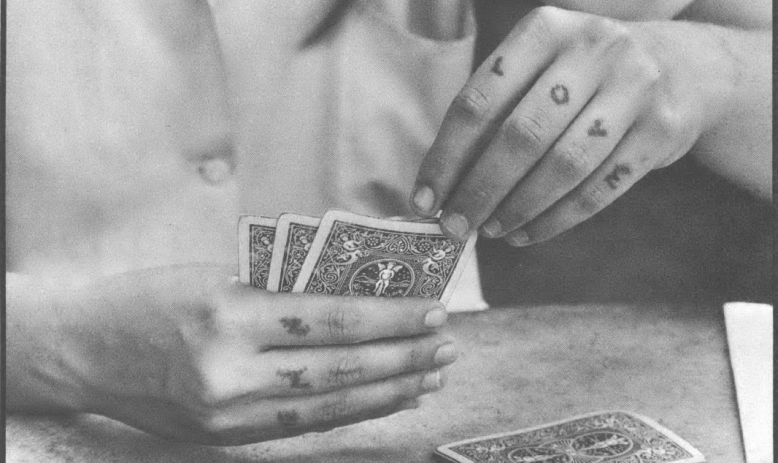 Black and white photo close-up of hands with tattooed knuckles holding a hand of cards