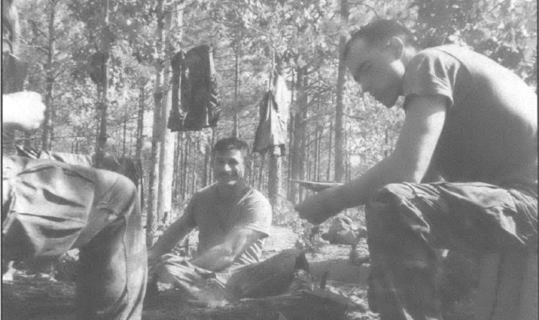 black and white photo of two white men in army wear in a forest next to a fire