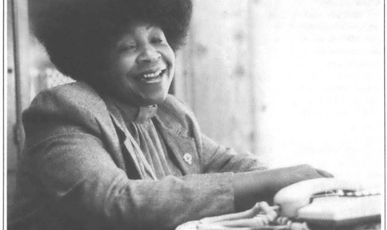 Photo of young Black woman seated at the table and laughing into the camera