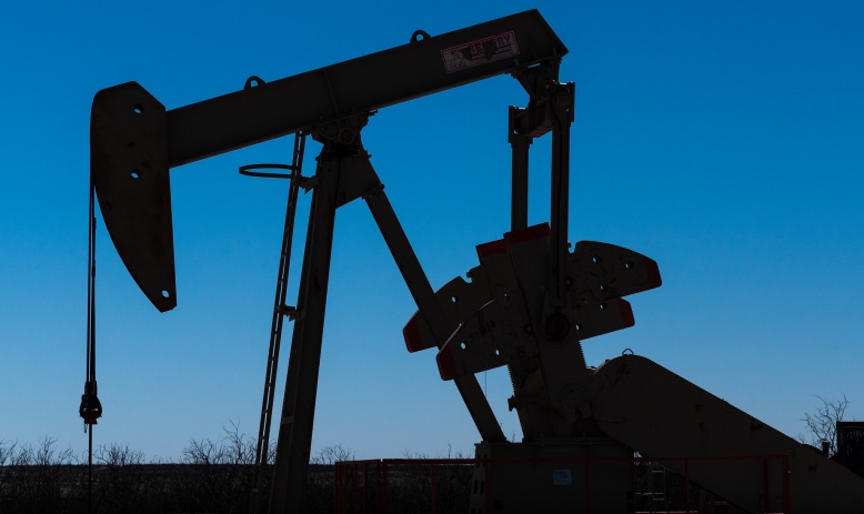 Silhouette of a pumpjack - a large metal lever-like machine - against a blue evening sky