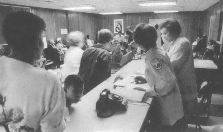 Black and white photo of people crowded around long tables