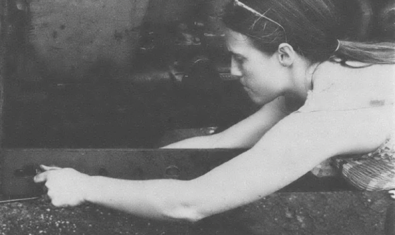 Black and white photo of woman stretched out and working on some kind of contraption