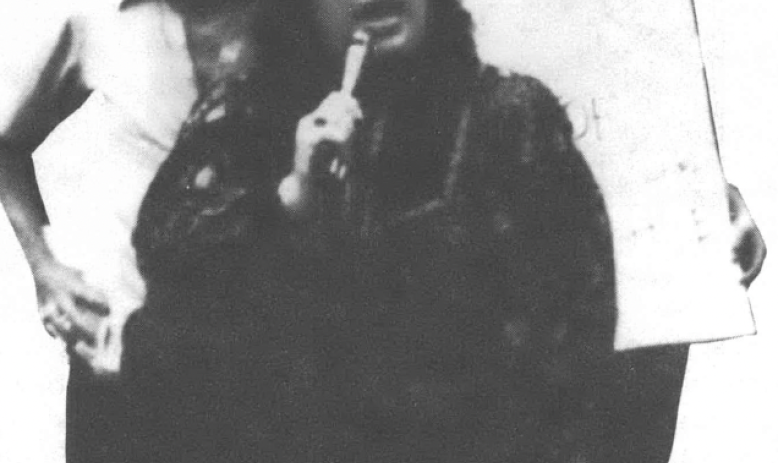 Black and white photo of three women, one of them speaking into a microphone