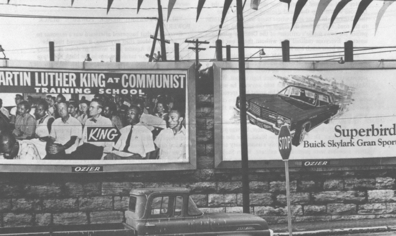 Black and white photo of truck parked in front of billboard that reads "Martin Luther King Communist Training School"