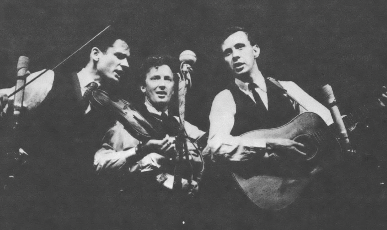 Black and white photo of three singing men around a microphone