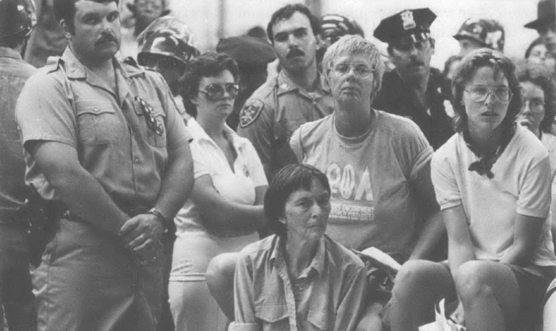 Picture of woman seated surrounded by people with hands clasped 