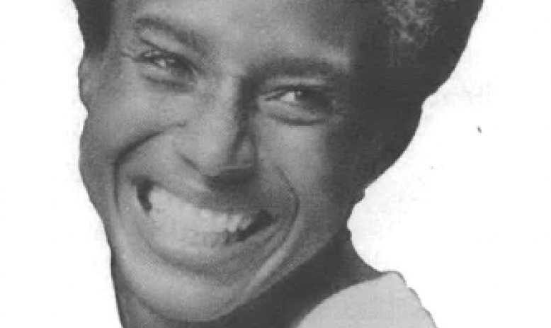 Black and white photo of Black woman with grey streaks in her hair smiling 