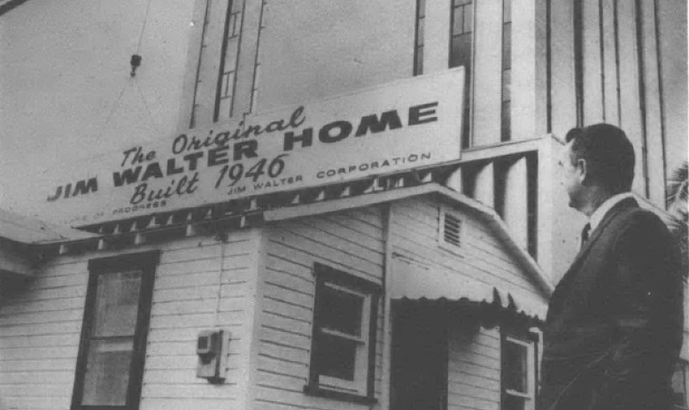 Black and white photo of man standing in front of sign on building reading "Jim Walter Homes"