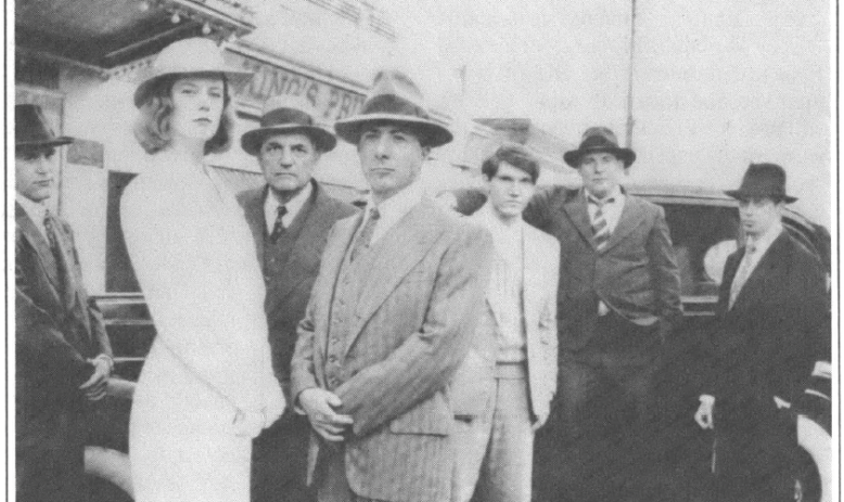 7 people posing seriously in suits and hats standing infront of cars and theater