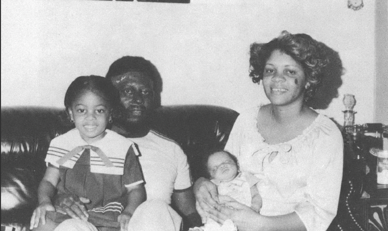 Black and white photo of Black family seated on couch smiling at camera