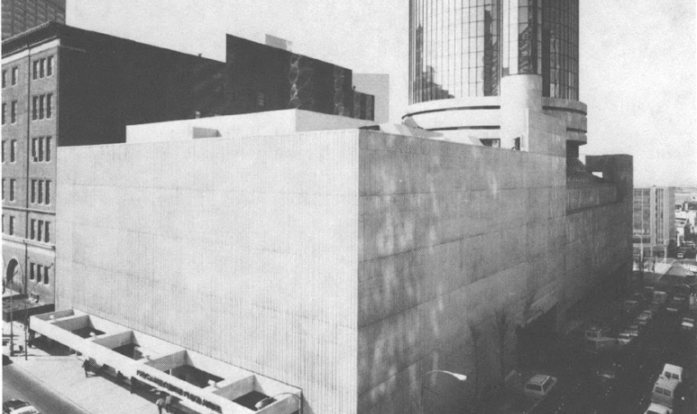 Black and white photo of building with glass-windowed tower that takes up entire city block