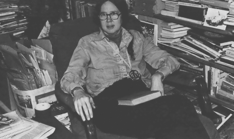 Black and white photo of woman reclining in chair surrounded by books