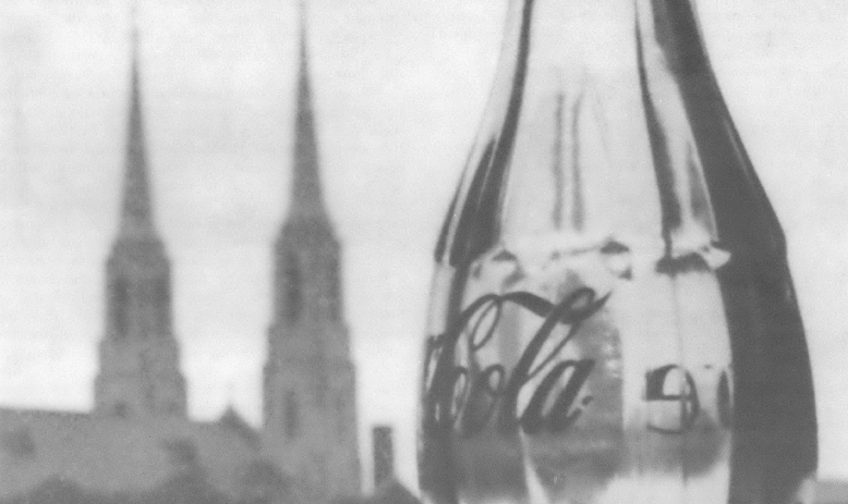 Black and white image of glass Coca-Cola bottle in front of church with two steeples