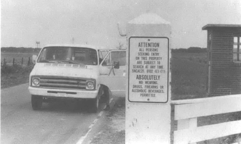 Black and white photo of white van pulling up to gate