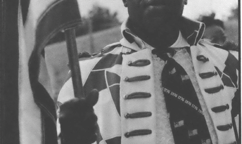 Black and white photo of Black man in ceremonial regalia holding an American flag