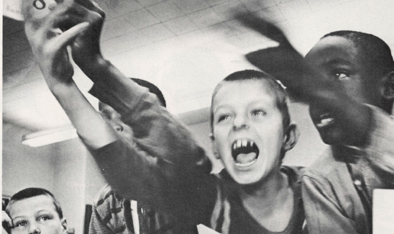 Black and white photo of young students yelling and reaching toward camera