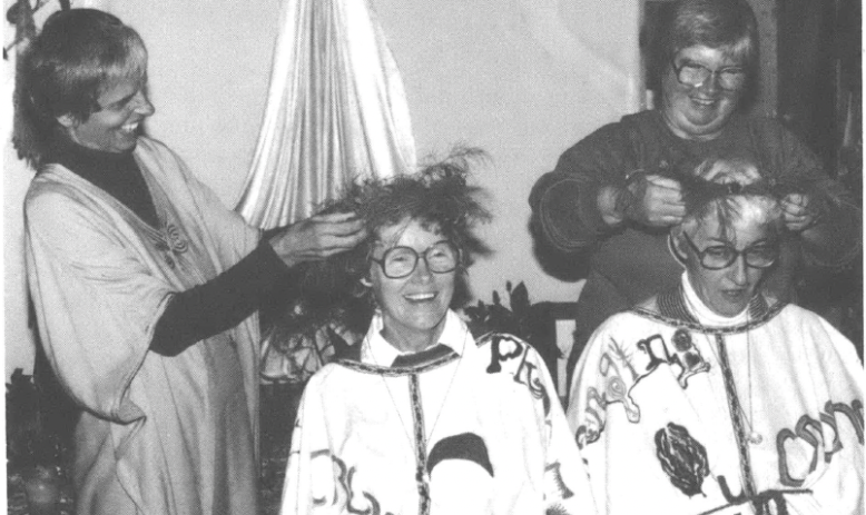 Photo of several white women smiling, one woman seated while others mess with her hair