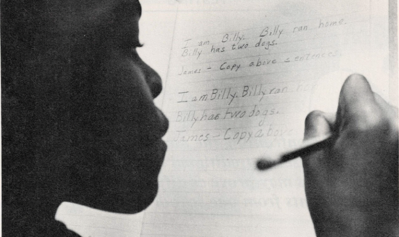 Black and white photo of young Black student writing on notebook paper