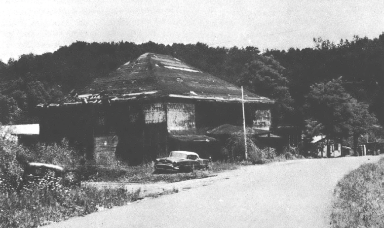 Black and white photo of building on side of the road with vehicle in front of it