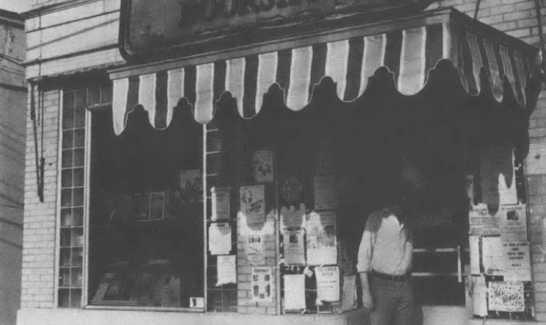 Black and white photo of front of Regulator Bookshop with awning and man standing in front of doorway