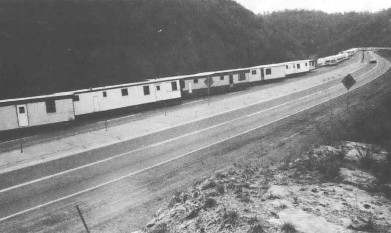 Black and white photo of single-wide trailers lined up along a mountain highway