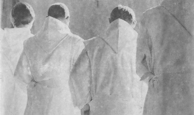 Black and white photo of three priests in white robes with back turned to camera