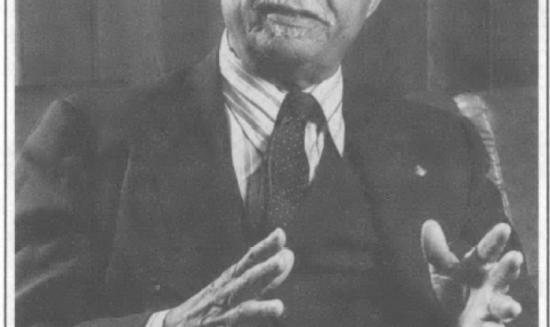 Man in a suit, bald, gesticulating with his hands, glasses, indoors