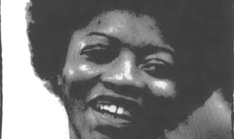 A black and white photo of Joan Little, a young Black woman smiling and wearing an Afro and collared shirt
