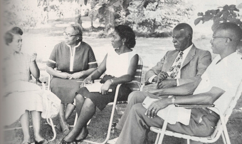 Black and white photo of group of people sitting in a circle outside