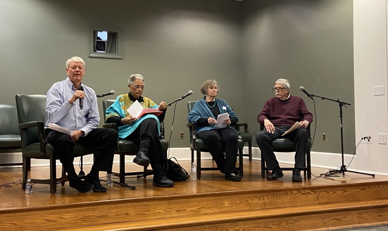 Four people sit on a stage in front of microphones