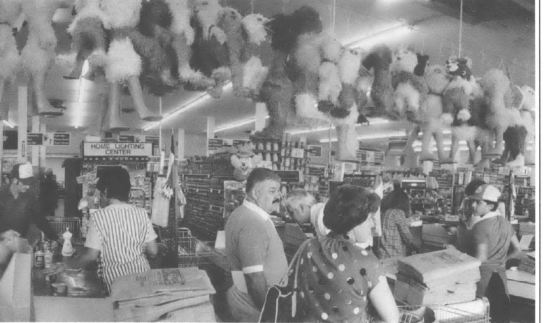 black and white lasndscappe photo of three check out aisles at a grocery store, with people checking out and a line of piñatas hanging over head from a line