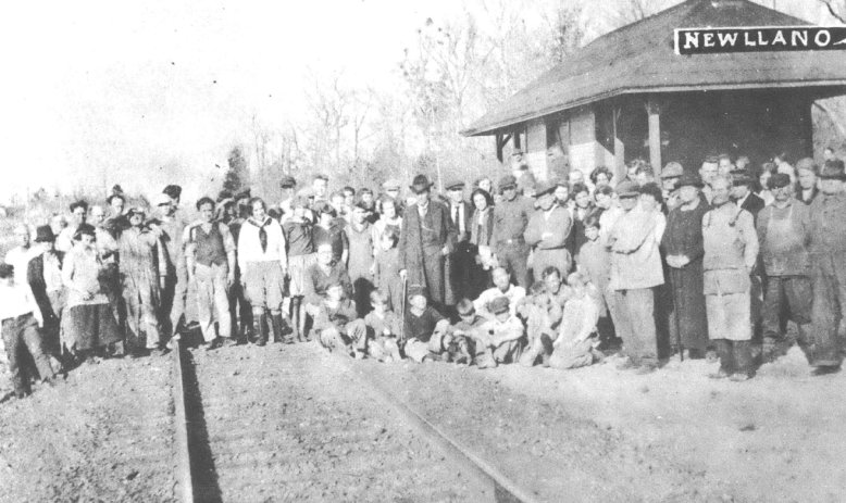 Black and white photo of crowd of people standing in front of railroad depot and across tracks