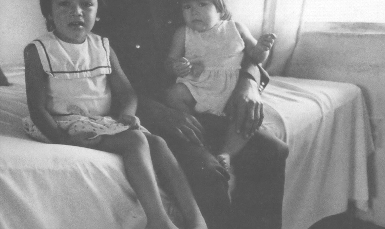 Black and white photo of man with two children sitting on bed