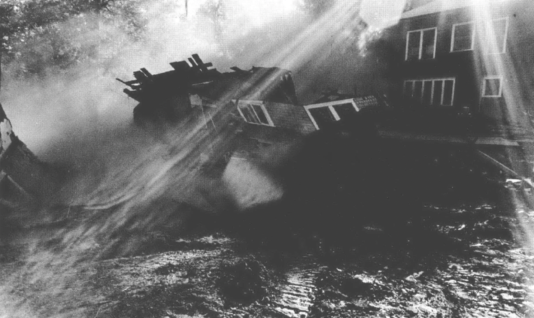 Black and white photo of fallen down house with a ray of sunshine hitting the wreckage