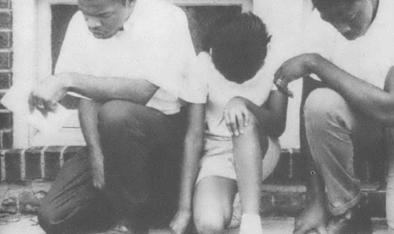 Black and white photo of John Lewis and two other young Black men kneeling on sidewalk