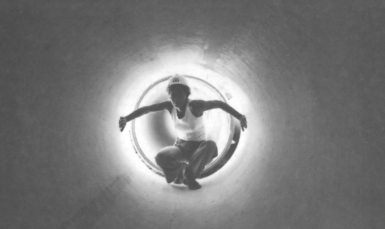 Black and white photo of woman in hard hat staring down pipe