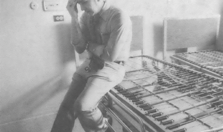 Black and white photo of man leaning against counter with hand on head