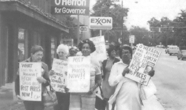 Black and white photo of people holding signs walking down a sidewalk