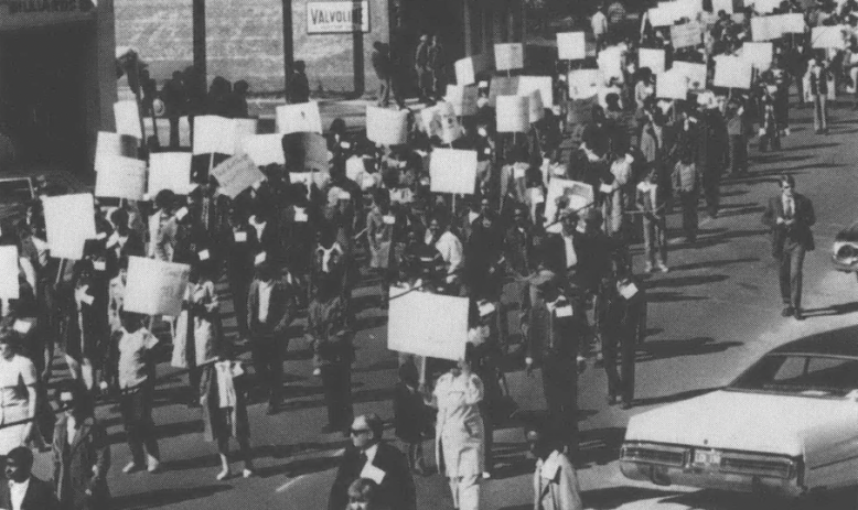 Black and white aerial view of protestors with signs marching down a street