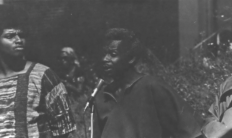 Black man speaks at a microphone as others look on