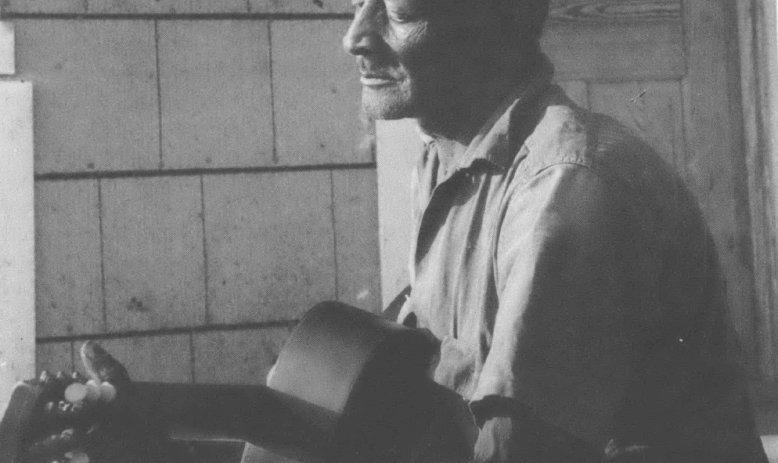 Black and white photo of Black man in hat playing guitar