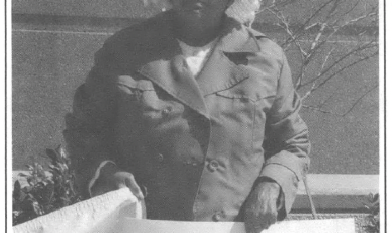 woman in a winter coat standing infront of a building with a sign that reads "We Need Houses! ACORN"