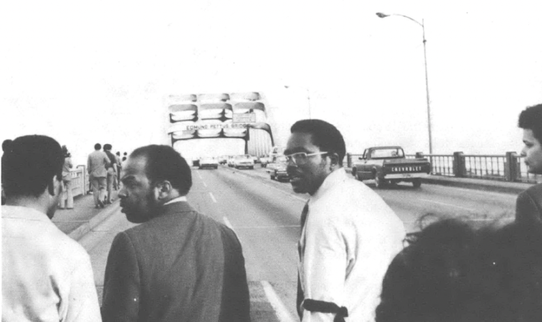 Black and white photo of John Lewis and others crossing the Edmund Pettus bridge