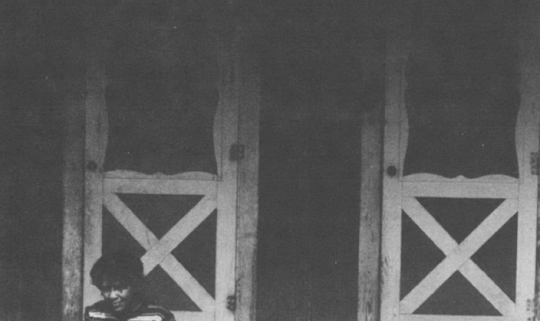 Black and white photo of person sitting on steps of house