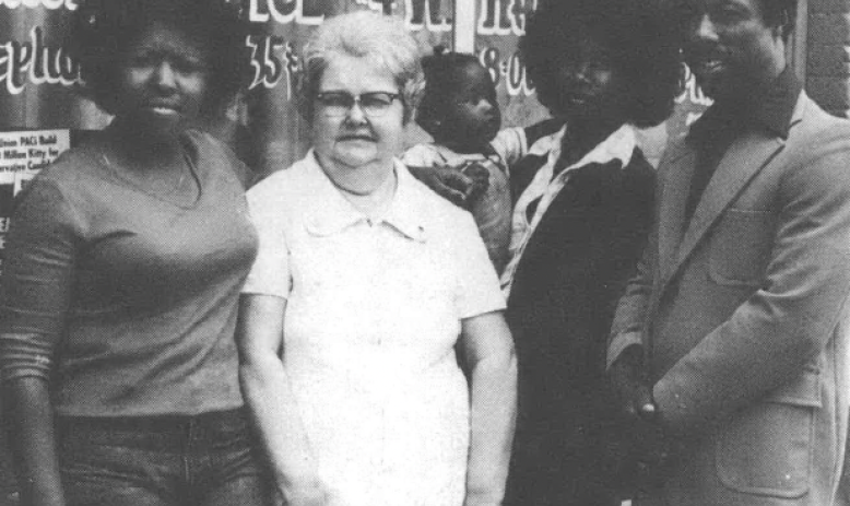 Black and white photo of women standing in front of a window