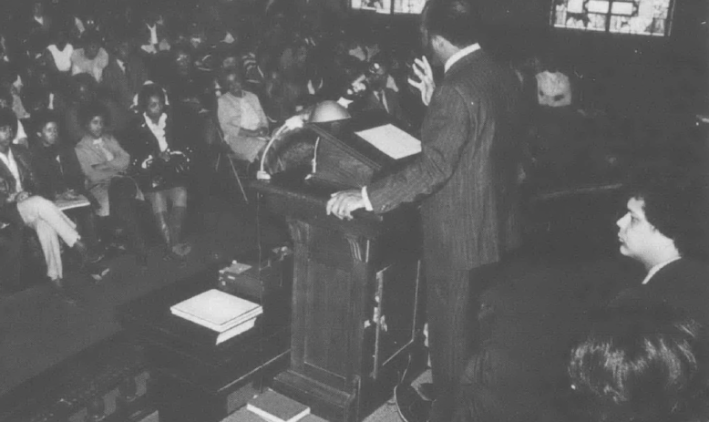 Black and white photo of John Lewis standing at podium speaking to a crowd of people in a church