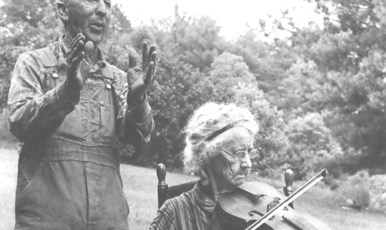 man clapping behind woman sitting and playing violin