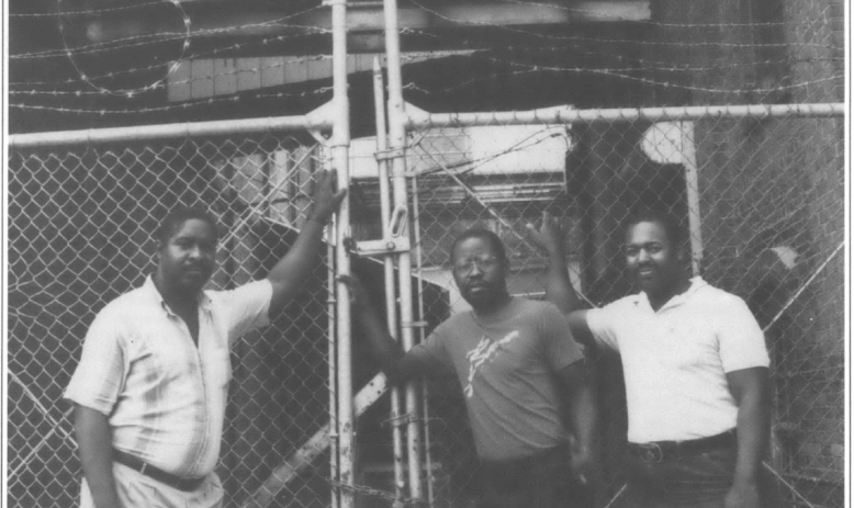 three men stand outside the gates of the American Tobacco factory