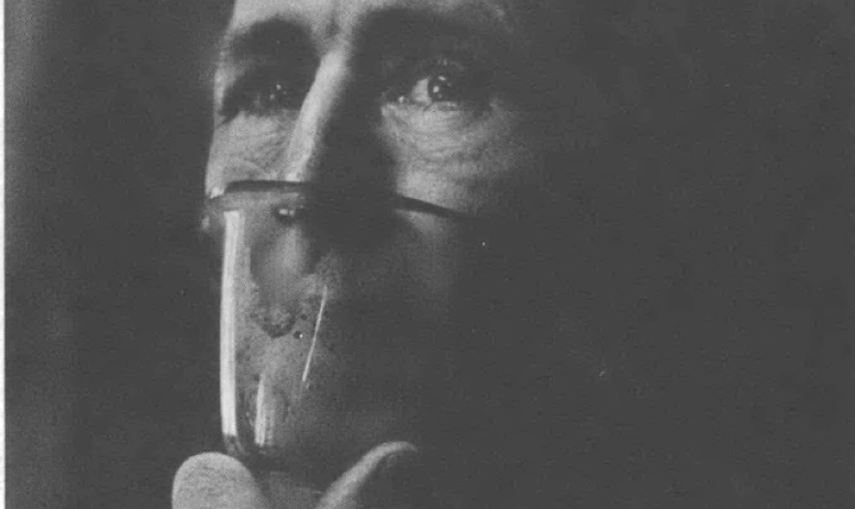 Black and white portrait of man with oxygen mask held up to his face