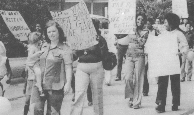 Black and white photo of several people marching down a street holding signs